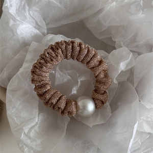 Detail of champagne glitter fabric scrunchie with elegant large white pearl accent