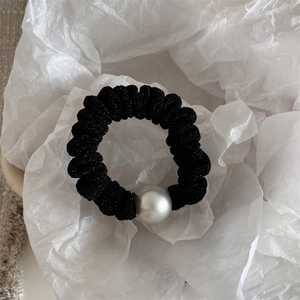 Macro shot of a black sparkling scrunchie with a large pearl on a white background