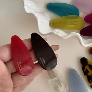 Close-up of handmade acetic acid teardrop hair clips with elegant gold logo engraving