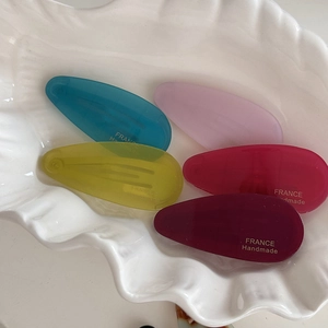 Close-up of five colorful acetate water-drop hair clips with France Handmade text in a shell tray