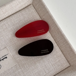 Detail view of red and black acetate teardrop hair clips with gold handmade lettering