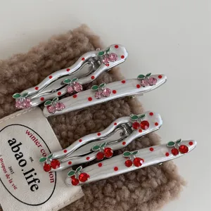 Close-up of alloy cherry hair clips with red rhinestones on soft brown fabric