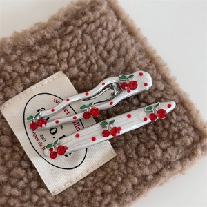 Detailed close-up of cherry hair clips with red rhinestones on a warm wool background