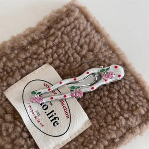 Close-up of a silver wavy hair clip with red polka dots and pink rhinestone cherries