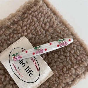 Detail of white resin hair clip featuring pink rhinestone cherries and red polka dots