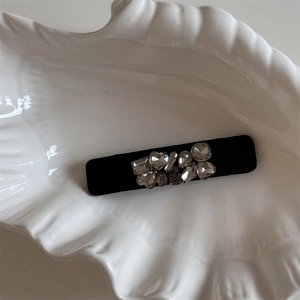 Detail of a velvet barrette with sparkling rhinestones in a white ceramic dish