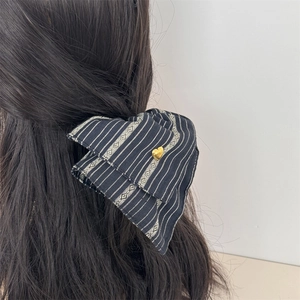 Close-up of a large black striped bow hair clip with a gold heart pendant on model