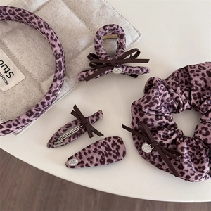 Détail d'accessoires cheveux imprimé léopard rose avec noeud en cuir et breloque dorée