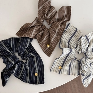 Close-up of three striped fabric scrunchies with heart-shaped gold charms in warm tones