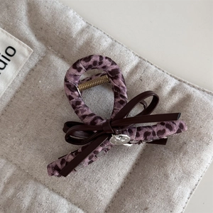 Vue détaillée d'une pince à cheveux léopard rose avec nœud en cuir sur fond en lin