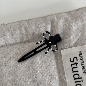 Dettaglio di un fermaglio nero a pois bianchi su tessuto strutturato beige