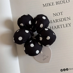 Close-up of black and white polka dot flower scrunchie with a heart-shaped tag charm