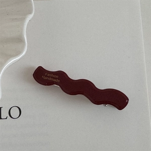 Close-up of deep red wavy resin hair clip with gold Fashion Handmade lettering detail
