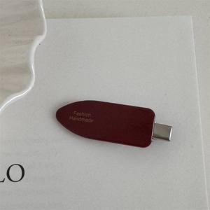 Detail of dark red oval hair clip with golden Fashion Handmade lettering and matte finish