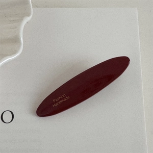 Detail of burgundy red oval hair clip with gold Fashion Handmade lettering and glossy finish