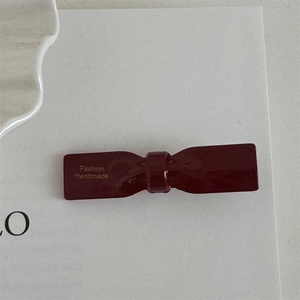Close-up of deep red handmade bow hair clip with gold text and glossy finish