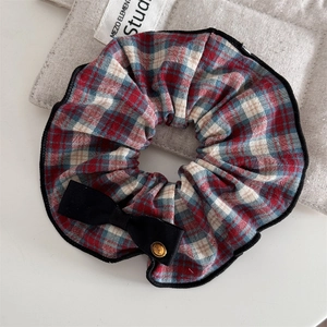 Close-up of vintage plaid hair scrunchie with a black bow and engraved gold button detail