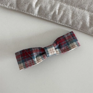 Detail of red and blue plaid bow hair clip on a minimalist neutral background