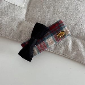 Detail of red and green plaid hair clip with a black bow and golden Love metal tag