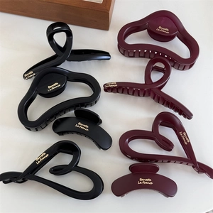 Pinze per capelli opache nere e bordeaux con scritte dorate su sfondo beige