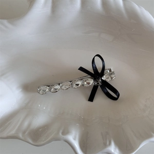 Détail macro d'une barrette en strass avec base argentée et petit nœud en satin noir