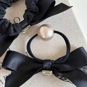 Detail of black satin bow scrunchie with crystal buckle and pearl hair tie on canvas