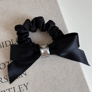 Detailed shot of a black satin bow hair tie with a central square cut crystal accent