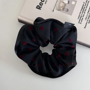 Detailed macro view of black fabric heart pattern scrunchie with brand logo tag