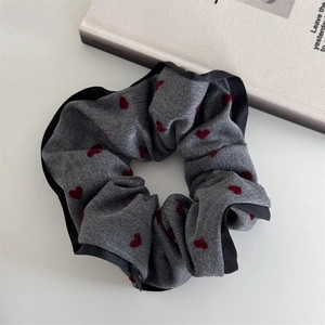 Detail of grey fabric hair scrunchie with red hearts, black satin trim on white background