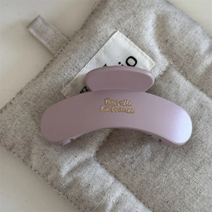 Dettaglio macro di molletta per capelli malva opaca con scritta dorata su lino