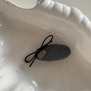 Vue macro montrant la texture en tweed gris et le nœud noir avec logo métallique sur le clip