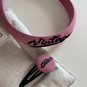 Close-up of pink fabric headband and hair clip with black vintage style embroidery