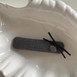 Détail de la barrette en tissu gris avec noeud en cuir et étiquette en métal sur plat