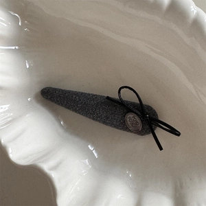 Détail de la pince à cheveux en tweed gris avec nœud noir et pendentif vintage en métal