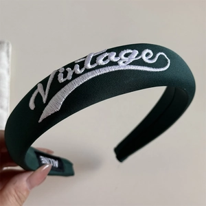 Close-up of a dark green embroidered headband featuring Vintage text and twill texture