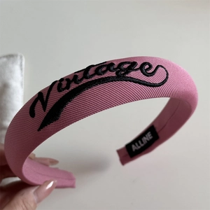 Close-up of pink fabric headband with vintage letter embroidery and brand label
