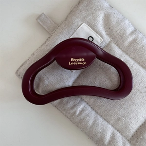 Dettaglio macro di una grande pinza per capelli bordeaux opaco con logo dorato