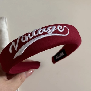 Close-up of wine red fabric headband with vintage embroidery and branding label