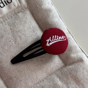Detailed close-up of dark red embroidered letter button on a black metal hair clip