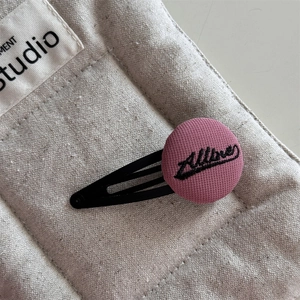 Detail of pink embroidered fabric button hair clip with black Allore lettering