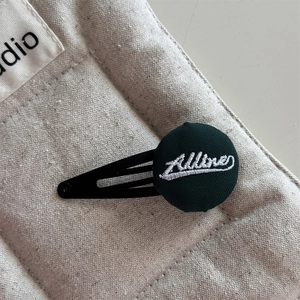 Detailed macro view of dark green fabric button hair clip with white letter embroidery