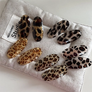 Polished leopard print oval hair clips set on a textured fabric pouch organizer