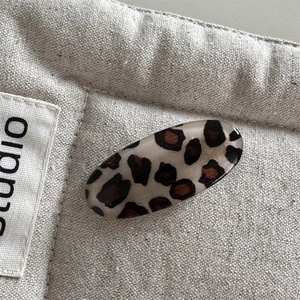 Close-up of leopard print oval hair clip with acetate texture on beige canvas fabric