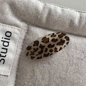Macro detail of oval leopard print hair clip with glossy texture on linen studio background