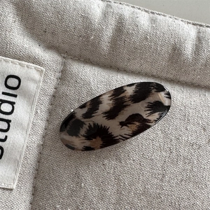 Close-up of leopard print oval hair clip with high-gloss finish on beige quilted fabric