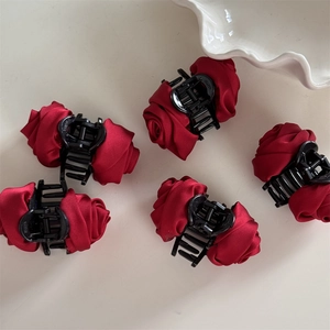 Five vintage deep red satin rose flower hair claws arranged on a light cream surface