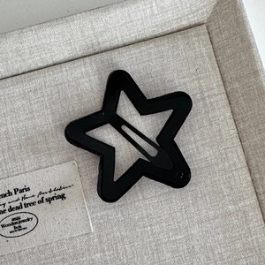 Close-up of a matte black star-shaped hair clip with a cut-out design on fabric surface