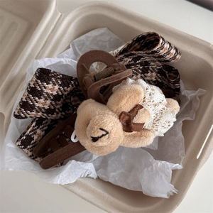 Détail d'une pince à cheveux ours avec nœud en pied-de-poule et dentelle dans un coffret