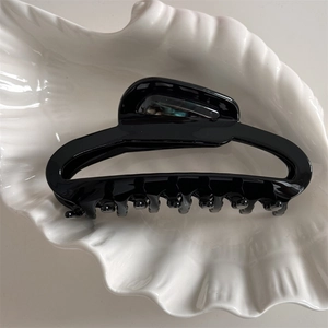 Top view of large black acetate hair claw clip on a white ceramic shell tray