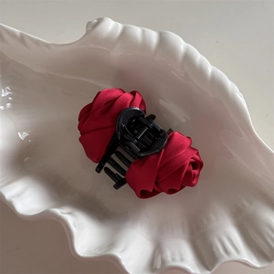 Detail view of a vintage dark red satin rose hair claw clip on a white shell plate